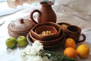 A still life arrangement of rustic clay pottery alongside fresh citrus fruits and white flowers.
