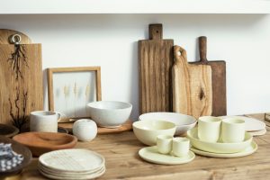 Set of minimalist light ceramic dishware and cutting boards arranged on wooden shelf in modern kitchen