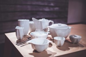 A stylish arrangement of white porcelain tableware including cups, bowls, and cutlery on a wooden table.