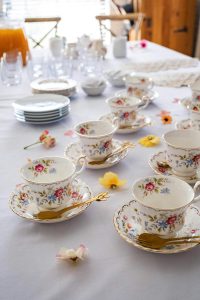 Beautifully arranged floral tea set with golden spoons on a table with a soft, airy feel.